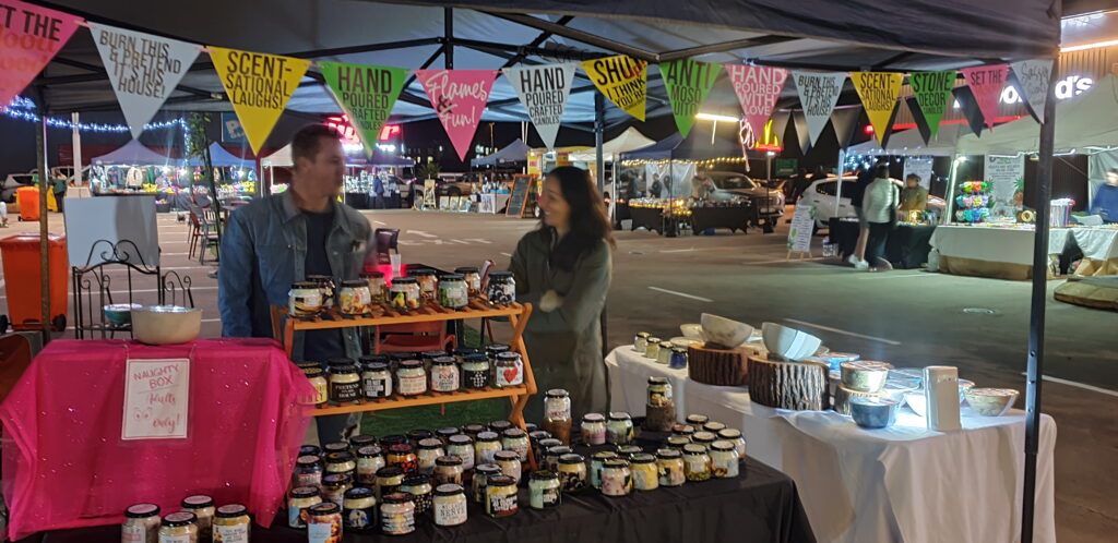 The Hand Poured Crafted Candles stall, displaying handmade candles at Cradlestone Mall Night Market with colorful bunting flags overhead.