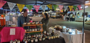 The Hand Poured Crafted Candles stall, displaying handmade candles at Cradlestone Mall Night Market with colorful bunting flags overhead.